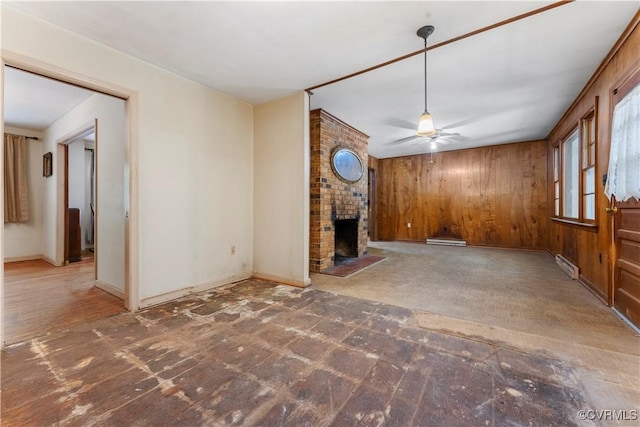 unfurnished living room featuring a fireplace, ceiling fan, wooden walls, and baseboards
