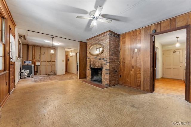 unfurnished living room with wooden walls, ceiling fan, and a brick fireplace