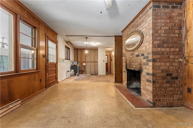 unfurnished living room with a baseboard radiator, wood walls, a fireplace, and brick patterned floors