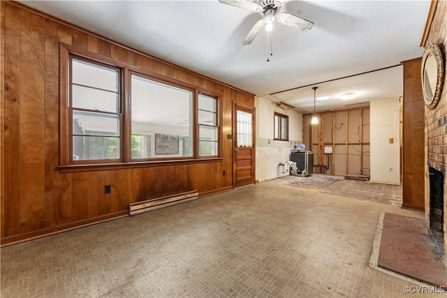 unfurnished living room with baseboard heating, wood walls, a fireplace, and ceiling fan
