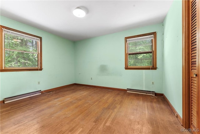 spare room featuring baseboard heating, plenty of natural light, light wood-style flooring, and baseboards
