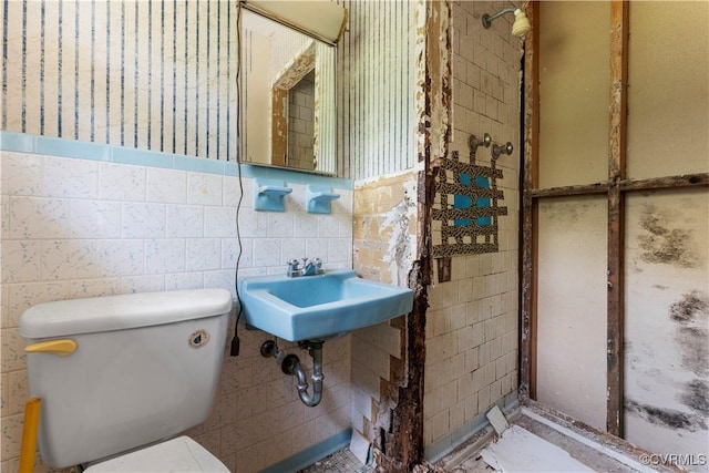 bathroom with toilet, tiled shower, and tile walls