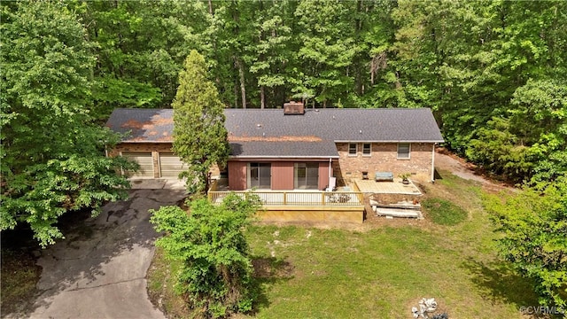 back of house with driveway, an attached garage, a chimney, a deck, and roof with shingles