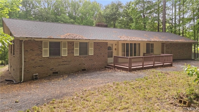 view of front of house with crawl space, a wooden deck, brick siding, a chimney, and roof with shingles