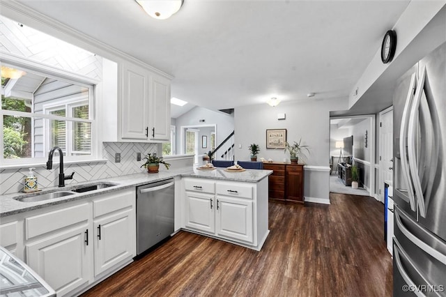 kitchen with stainless steel appliances, a sink, a peninsula, tasteful backsplash, and dark wood-type flooring