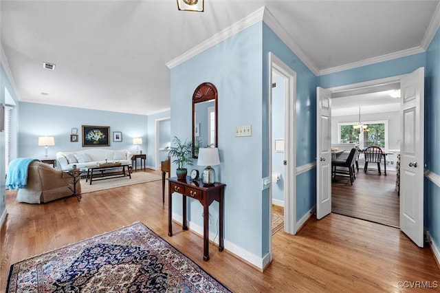 corridor with light wood-style floors, crown molding, baseboards, and a chandelier