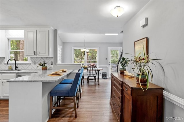 kitchen with a sink, wood finished floors, white cabinets, and a breakfast bar area