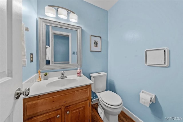 half bath with toilet, vanity, wood finished floors, and baseboards