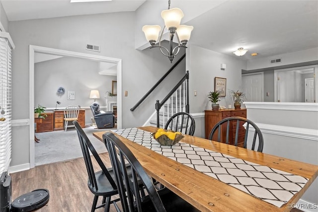 dining room with a chandelier, wood finished floors, a lit fireplace, vaulted ceiling, and stairway