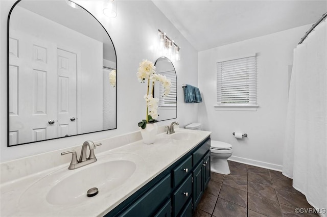 bathroom featuring toilet, double vanity, and baseboards