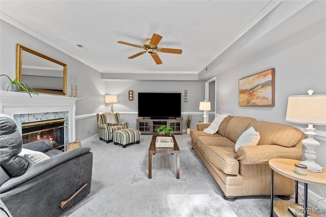 carpeted living room with a ceiling fan, crown molding, and a high end fireplace