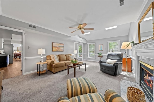 carpeted living area with a premium fireplace, baseboards, a ceiling fan, and ornamental molding