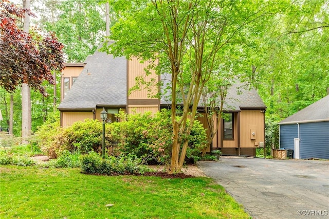 view of front of house with driveway, a shingled roof, and a front lawn