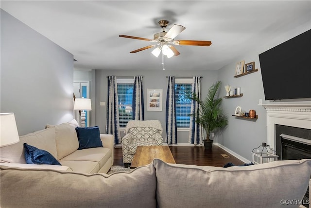 living room featuring a ceiling fan, a glass covered fireplace, wood finished floors, and baseboards