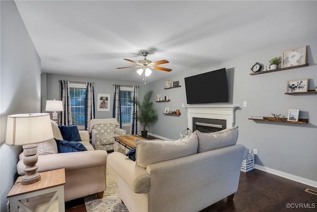 living room with a ceiling fan, a fireplace, baseboards, and dark wood-style floors