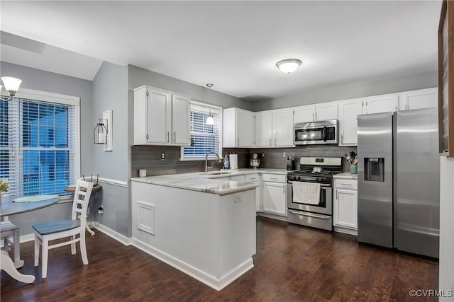 kitchen with stainless steel appliances, a sink, a peninsula, dark wood-style flooring, and backsplash