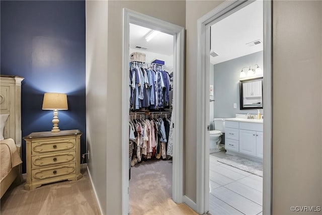 bedroom with a closet, a walk in closet, a sink, ensuite bathroom, and baseboards
