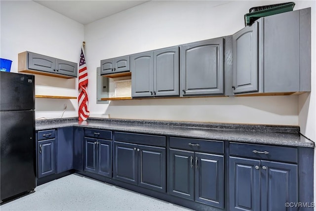 kitchen with freestanding refrigerator, dark countertops, blue cabinetry, and open shelves