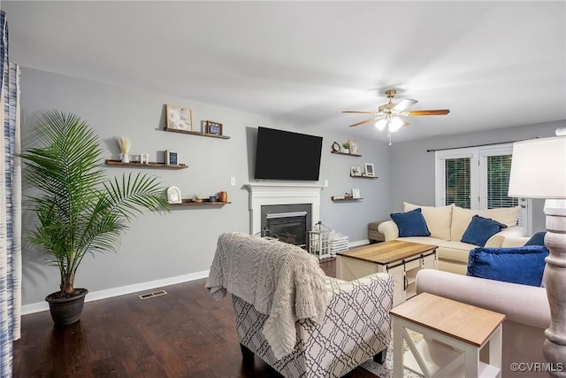 living room featuring baseboards, a ceiling fan, wood finished floors, and a glass covered fireplace