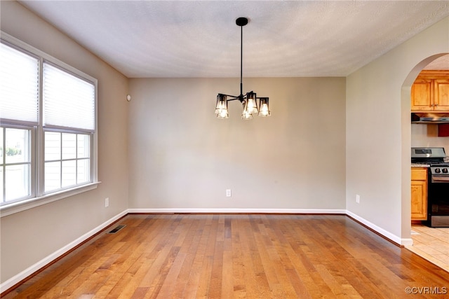 unfurnished room featuring a chandelier, arched walkways, light wood-type flooring, and baseboards