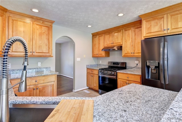 kitchen featuring appliances with stainless steel finishes, arched walkways, under cabinet range hood, recessed lighting, and light stone countertops