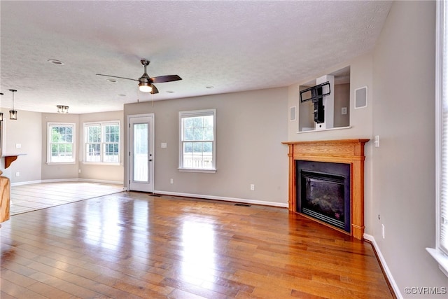 unfurnished living room with a textured ceiling, a glass covered fireplace, wood finished floors, ceiling fan, and baseboards