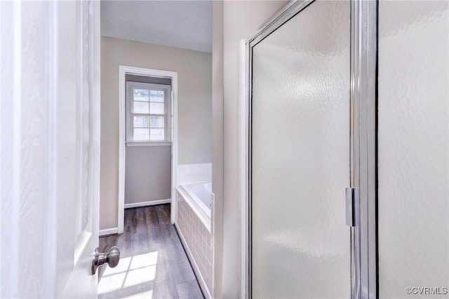 full bath with wood finished floors, a shower stall, a garden tub, and baseboards