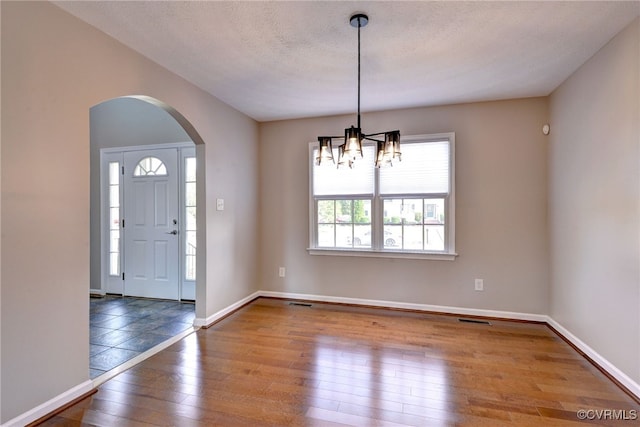 entrance foyer with arched walkways, a chandelier, hardwood / wood-style flooring, and baseboards