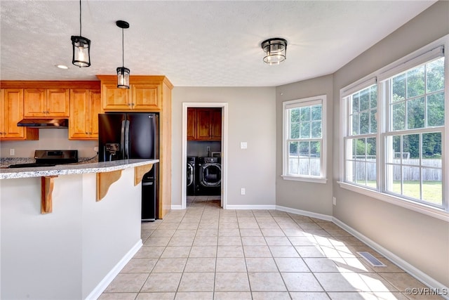 kitchen with under cabinet range hood, black fridge with ice dispenser, washer and dryer, a breakfast bar, and electric stove