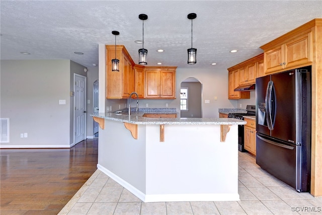 kitchen featuring black fridge with ice dispenser, stainless steel range with gas cooktop, a peninsula, under cabinet range hood, and arched walkways