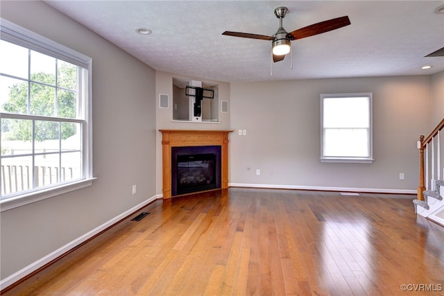 unfurnished living room with stairway, wood-type flooring, baseboards, a ceiling fan, and a glass covered fireplace