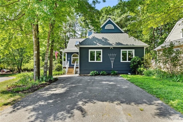 view of front of home featuring asphalt driveway, a chimney, a shingled roof, and covered porch