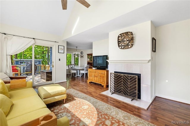living area with wood finished floors, baseboards, a tile fireplace, a ceiling fan, and high vaulted ceiling