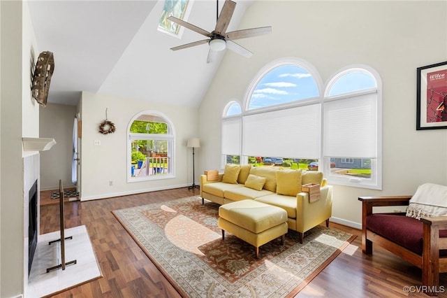 living area featuring high vaulted ceiling, ceiling fan, wood finished floors, a fireplace with flush hearth, and baseboards