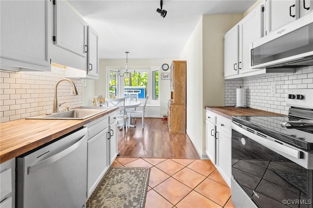 kitchen with stainless steel appliances, butcher block countertops, a sink, tasteful backsplash, and white cabinets