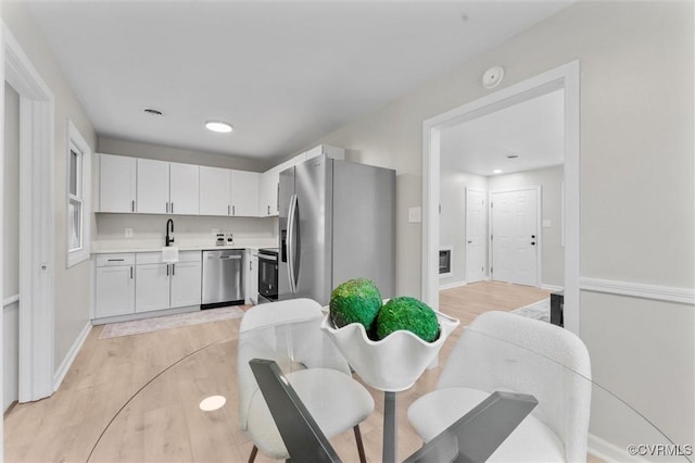 kitchen with stainless steel appliances, white cabinets, light countertops, light wood-style flooring, and a sink