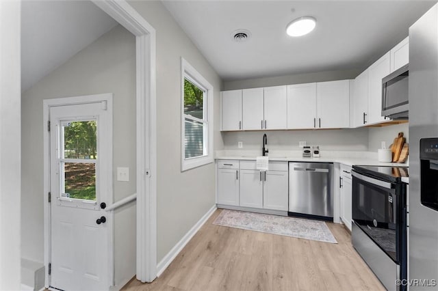 kitchen with appliances with stainless steel finishes, light wood-style flooring, light countertops, white cabinets, and a sink