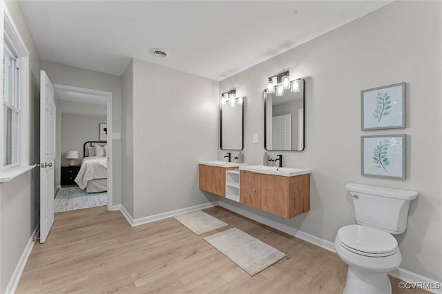 bathroom with wood finished floors, toilet, baseboards, double vanity, and ensuite bathroom