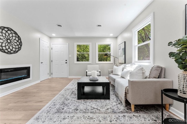 living area with wood finished floors, baseboards, recessed lighting, and a glass covered fireplace
