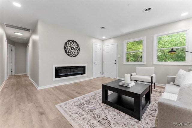 living room with light wood-type flooring, baseboards, recessed lighting, and a glass covered fireplace