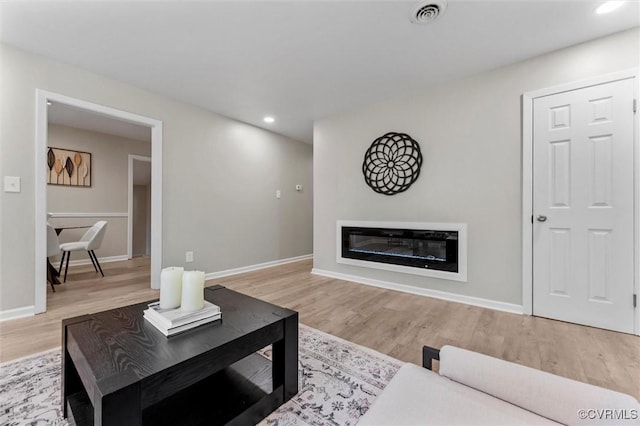 living room featuring wood finished floors, recessed lighting, baseboards, and a glass covered fireplace