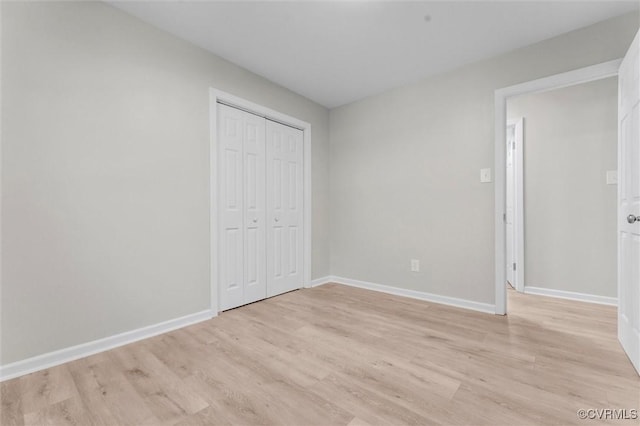 unfurnished bedroom featuring light wood-style floors, baseboards, and a closet