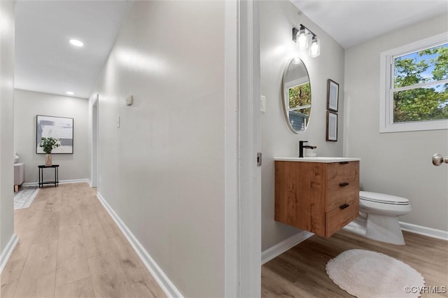 bathroom featuring wood finished floors, toilet, vanity, baseboards, and recessed lighting