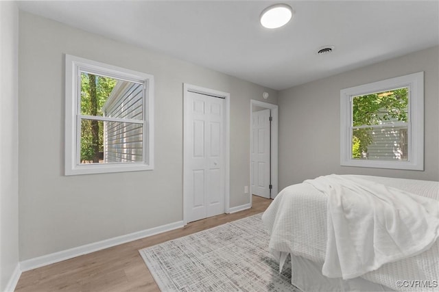 bedroom with multiple windows, light wood finished floors, baseboards, and a closet