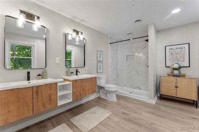 bathroom with wood finished floors, toilet, a marble finish shower, and two vanities