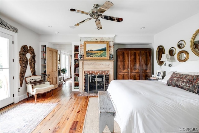 bedroom featuring multiple windows, light wood-style floors, a fireplace, and ceiling fan