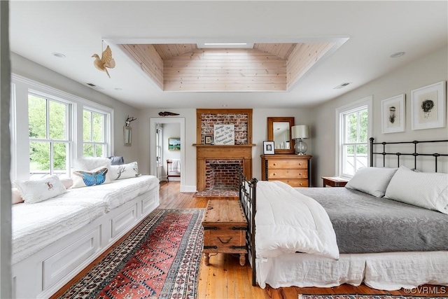 bedroom with a raised ceiling, light wood-style floors, and a brick fireplace