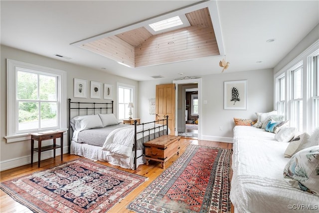 bedroom featuring a skylight, light wood-type flooring, a tray ceiling, and wooden ceiling