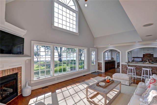 6454 Carmines Island Ln, Gloucester, VA 23072 - living area featuring a brick fireplace, high vaulted ceiling, wood finished floors, arched walkways, and baseboards