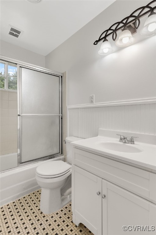 bathroom featuring wainscoting, toilet, vanity, and enclosed tub / shower combo